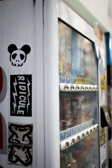 Close-up of a vending machine featuring drinks and artistic stickers in an urban setting.