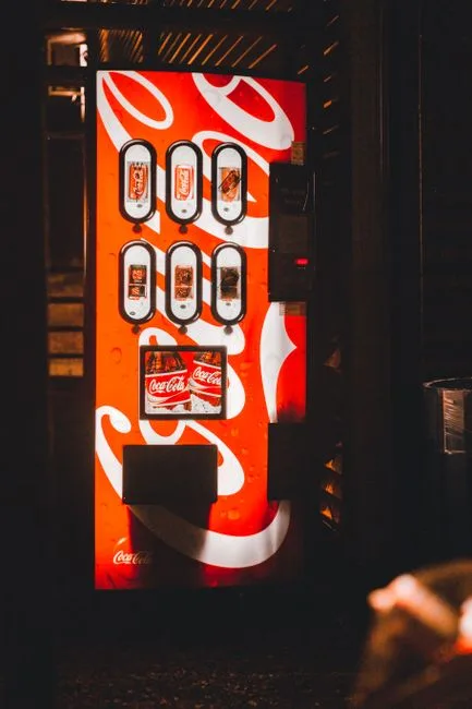 A bright vending machine offering cold drinks, showcasing iconic branding in a dimly lit area.