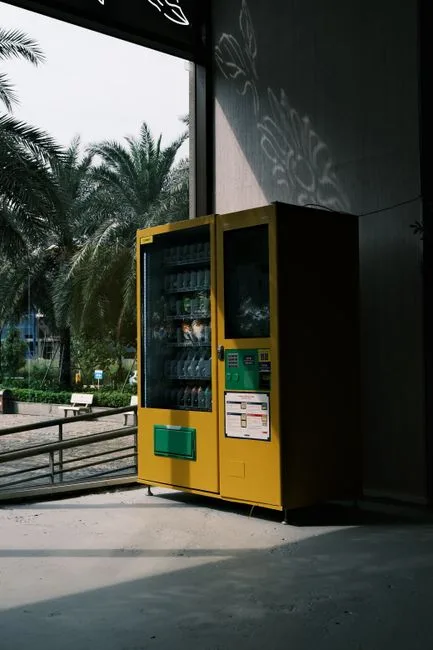 Yellow vending machine indoors with palm trees outside, dramatic lighting.