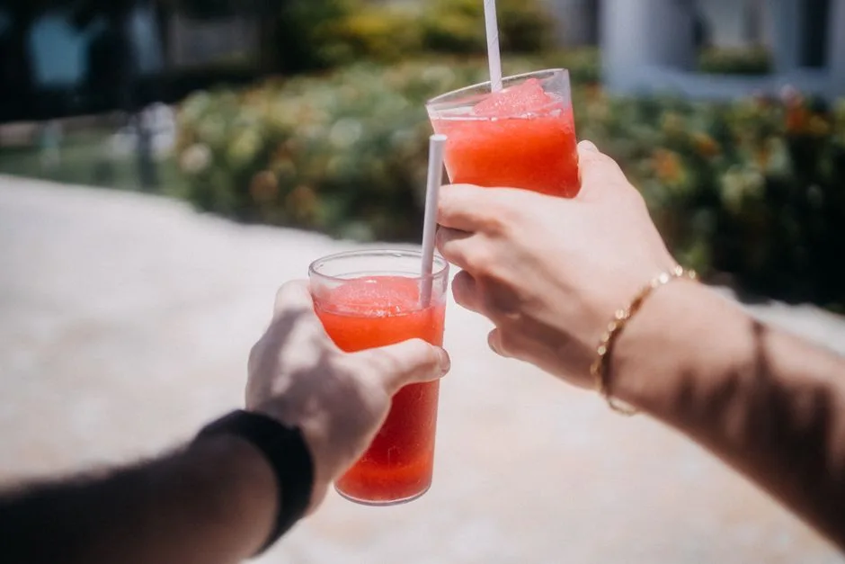 Two hands clinking refreshing red slushy drinks outdoors, symbolizing summer fun and refreshment.