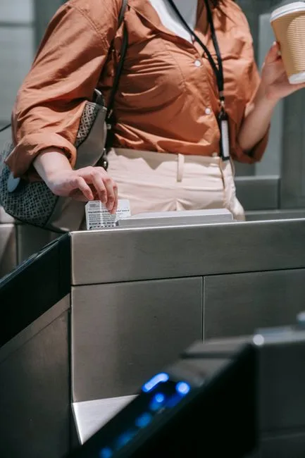 Woman swipes card at subway turnstile, holding coffee to-go. Urban transit scene.