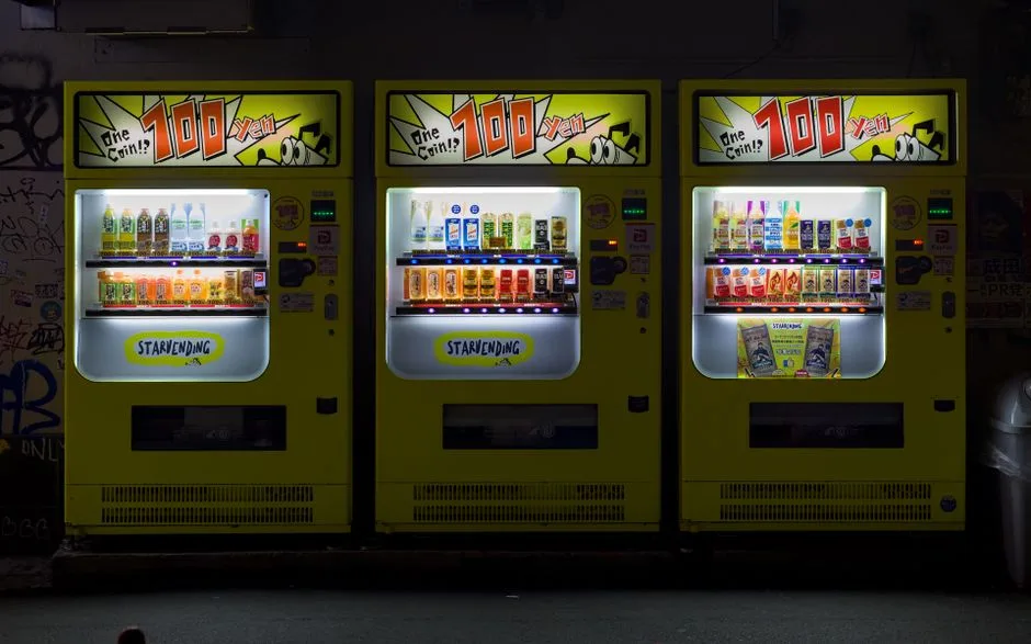 Three brightly lit vending machines on an urban street in Osaka, Japan at night.
