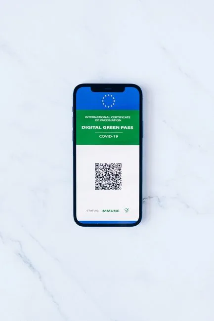 A smartphone displaying a digital green pass with QR code on marble surface.