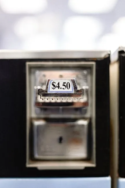 Cash dispenser made of stainless steel with small rectangular signboard representing digits and symbols of dot and dollar on blurred background