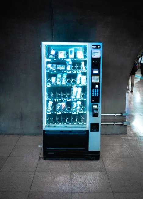 A glowing vending machine stocked with various products in a dimly lit corridor.