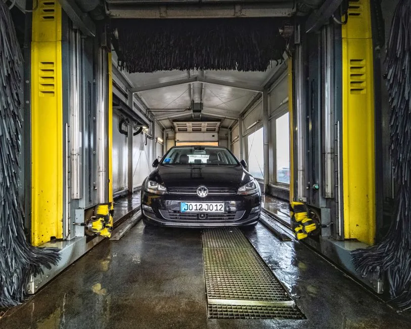 A black car undergoing a thorough cleaning in an automated car wash facility.