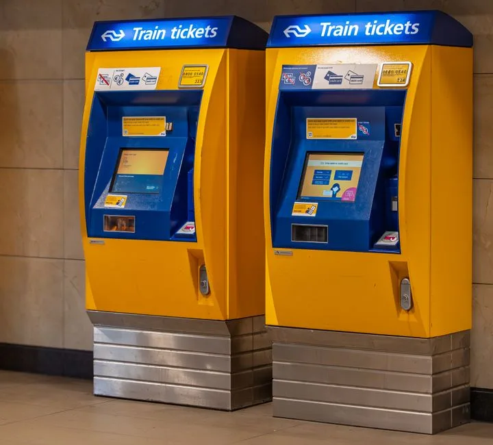 Two vibrant yellow and blue train ticket machines in an indoor station setting.
