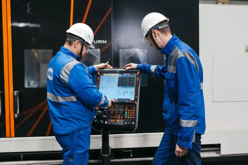 Two engineers operating CNC machinery in a factory setting, wearing safety gear and uniforms.