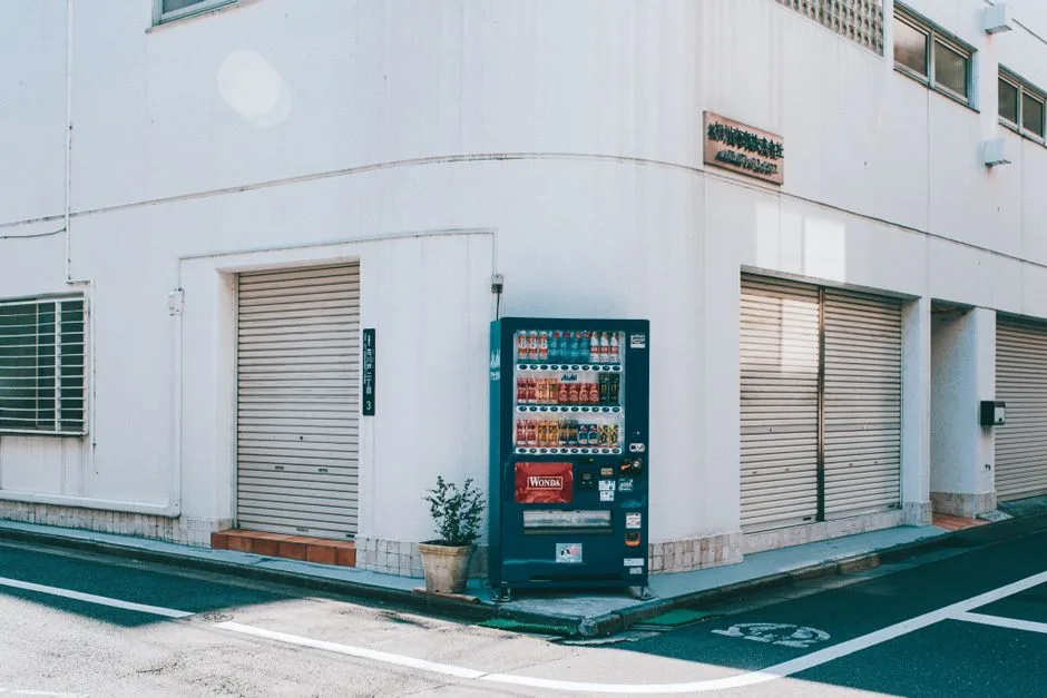 A quiet urban street corner featuring a vending machine against a white building.