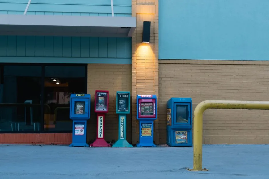 Row of colorful newspaper stands against a brick wall in urban setting during daytime.