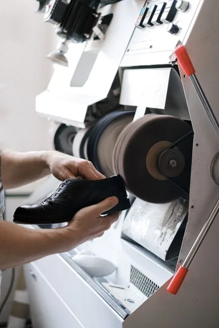 Close-up of craftsman polishing a leather shoe using industrial machinery indoors.