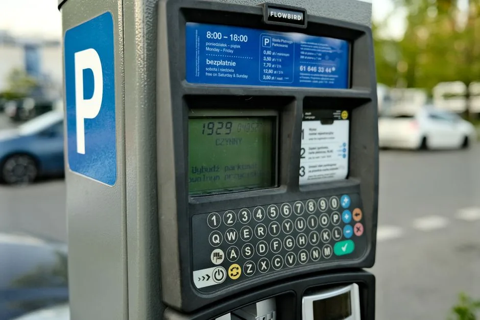 Close-up of a digital parking meter in a city setting with cars in the background.