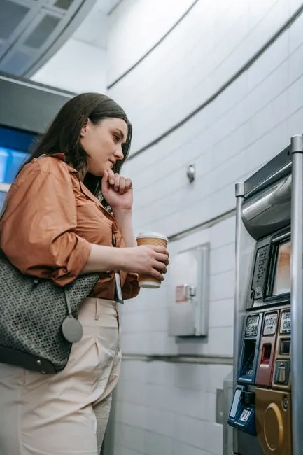 A young woman at a subway station uses a vending machine to purchase a ticket.