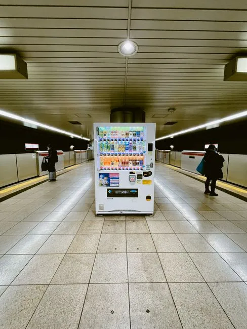 Vending machine in a Tokyo subway station with commuters on the platform.