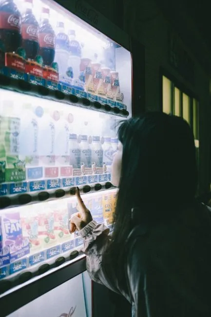 A woman selecting a drink at a brightly lit vending machine at night.