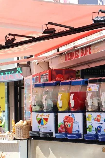 Colorful slush machines at an outdoor vendor stand offering a variety of frozen drinks.